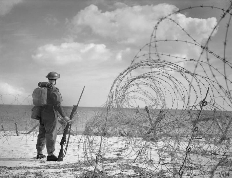 A soldier stands near barbed wire on a British beach during World War 2