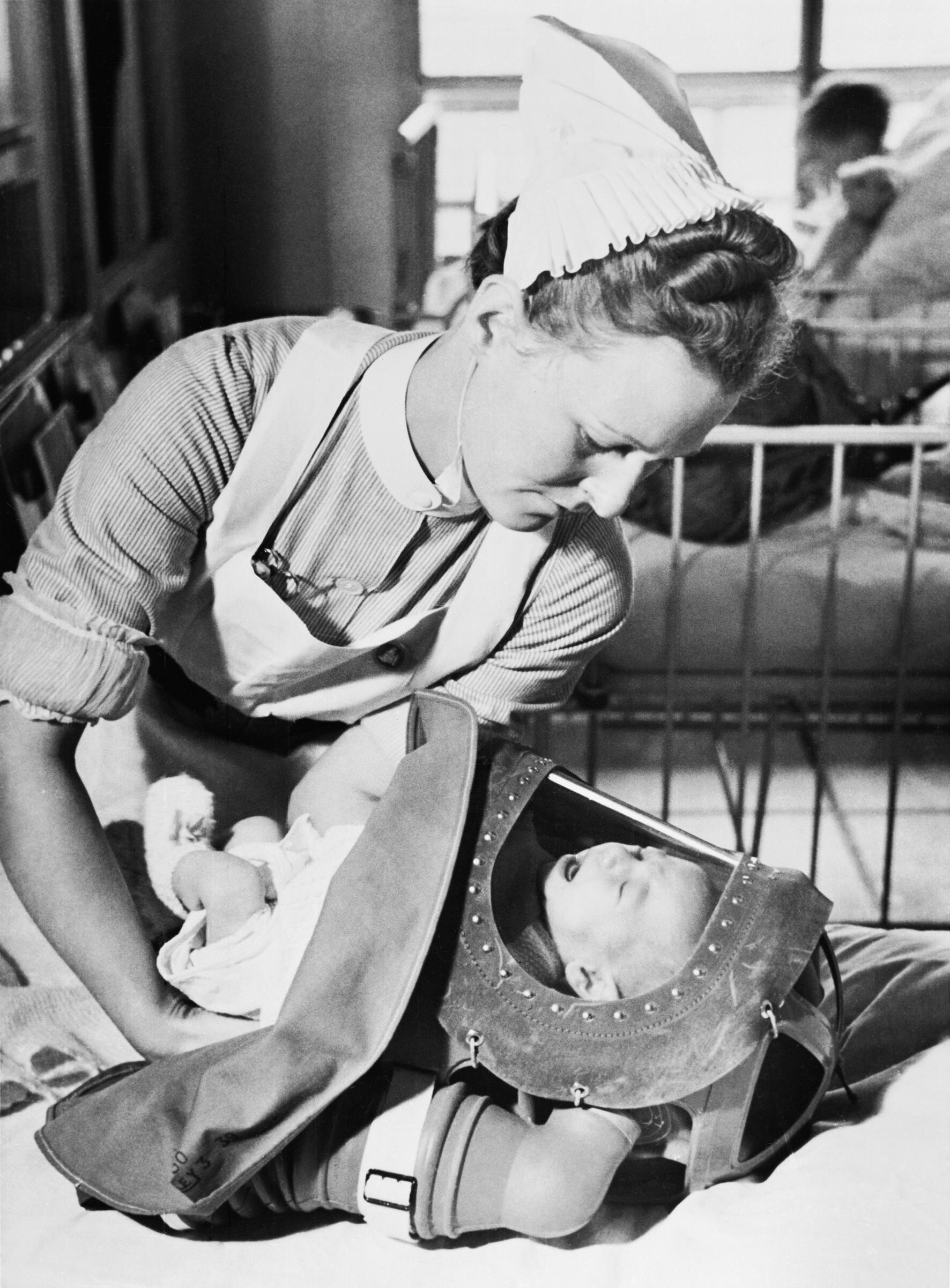 black and white photo of a nurse putting a baby in a baby gas mask during a drill