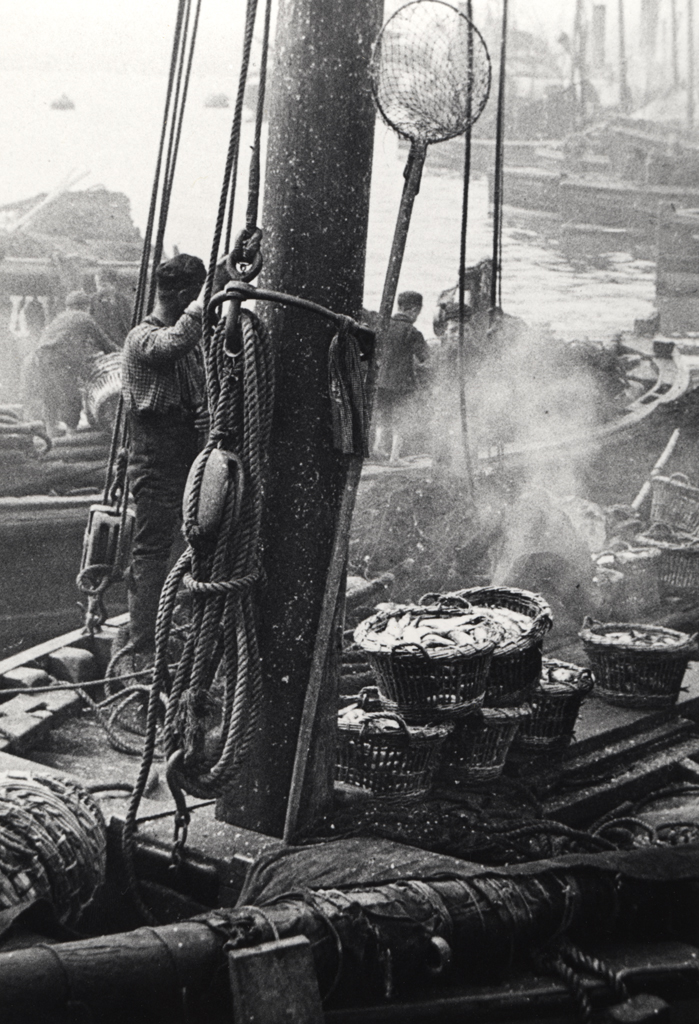 black and white photo of a fishing boat with baskets of fish on deck waiting to be unloaded