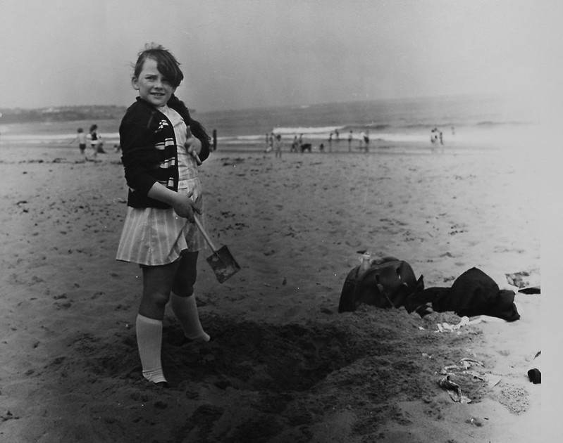 Photo showing a girl standing on a beach holding a spade