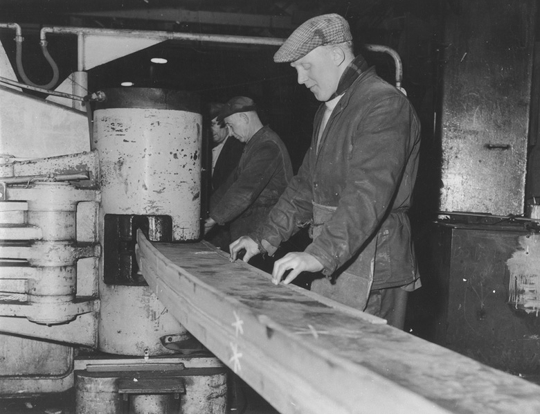 black and white photo of shipyard workers using a bending machine